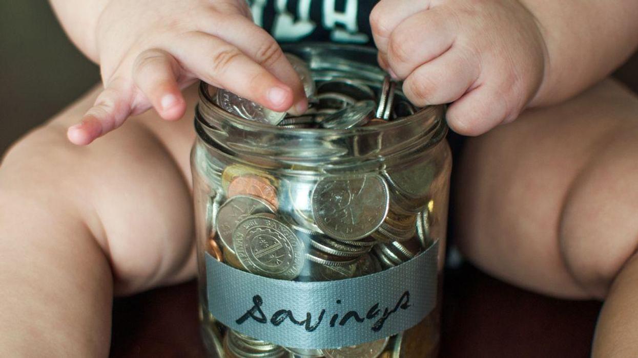 A baby boy is holding a jar filled with coins.