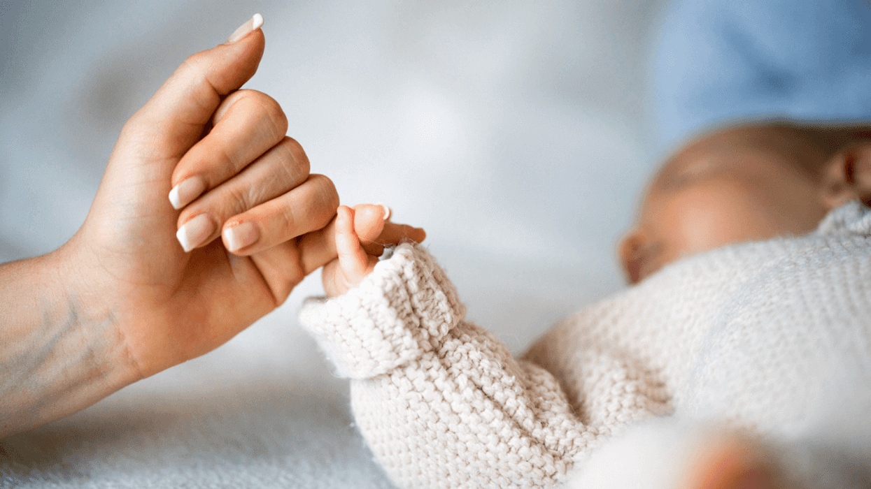 A baby holding a woman's pinky finger.