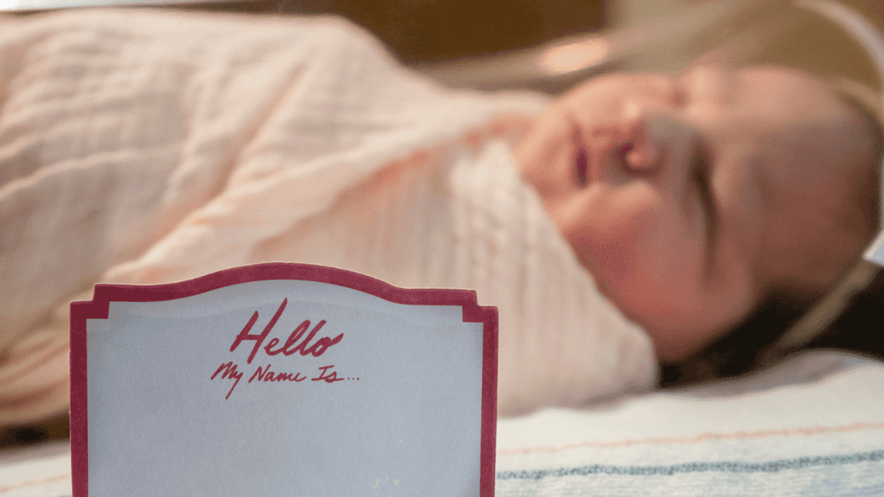A baby in a hospital crib with a blank name tag on the side.
