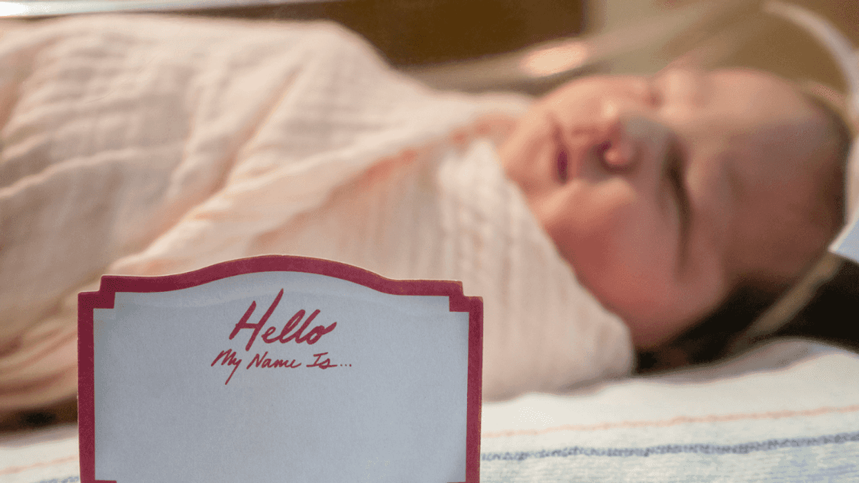 A baby in a hospital crib with a "hello my name is" sticker on it.
