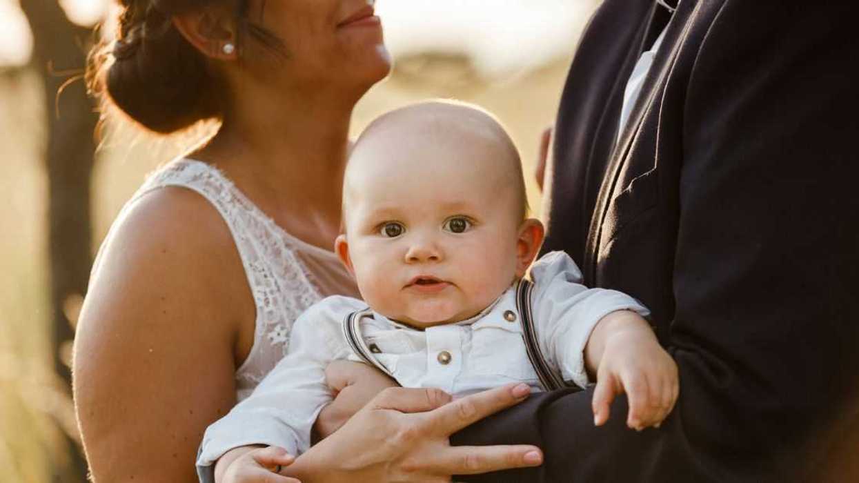 A baby is held by a bride and groom