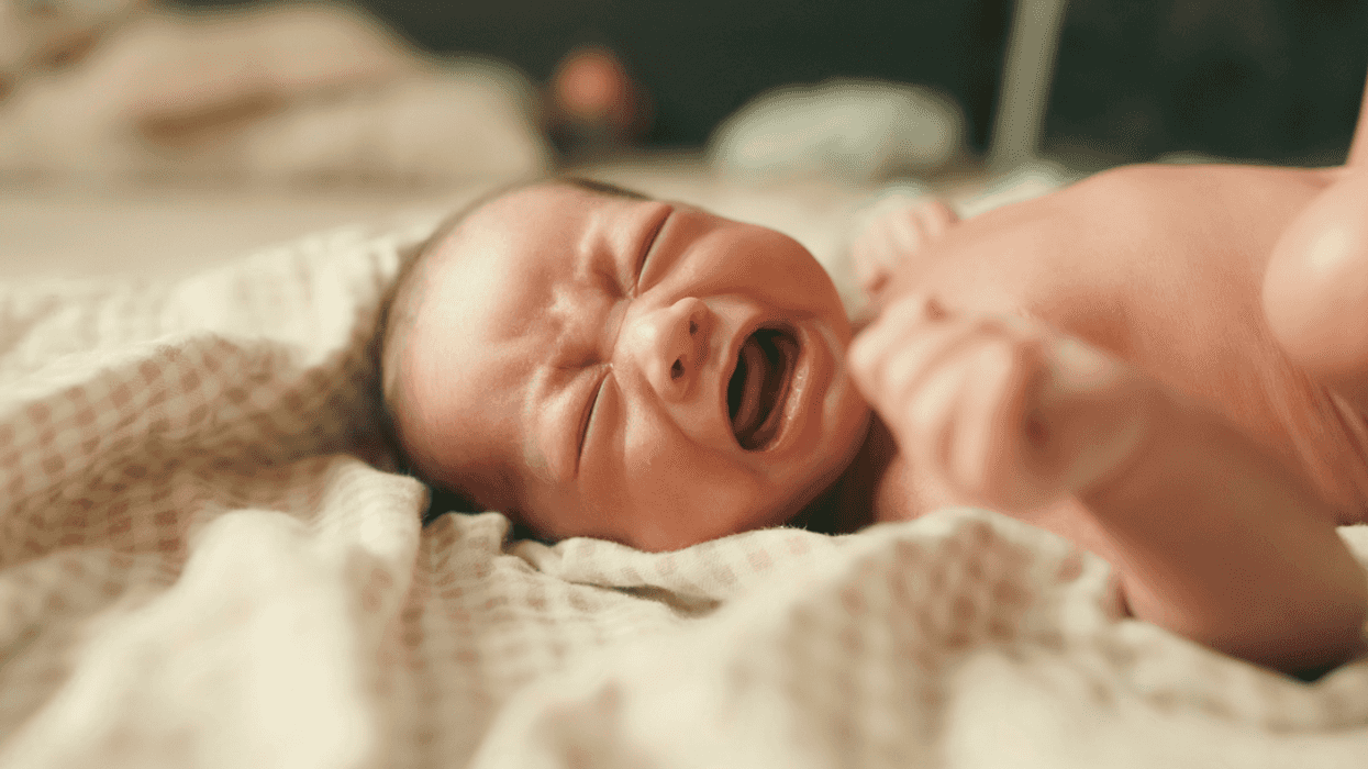 A baby lying on a bed an crying.