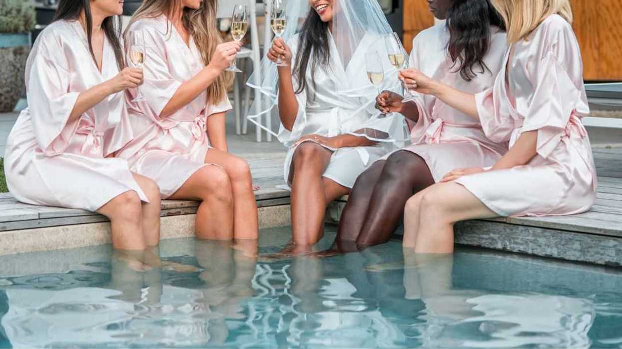 A bachelorette pool party, showcasing diverse friends in silk bathrobes, toasting with champagne and dipping their legs in the refreshing pool.