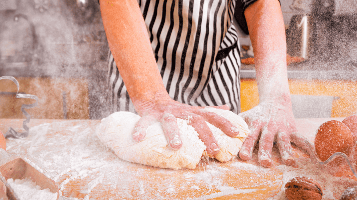 A baker kneading dough with flour flying everywhere.