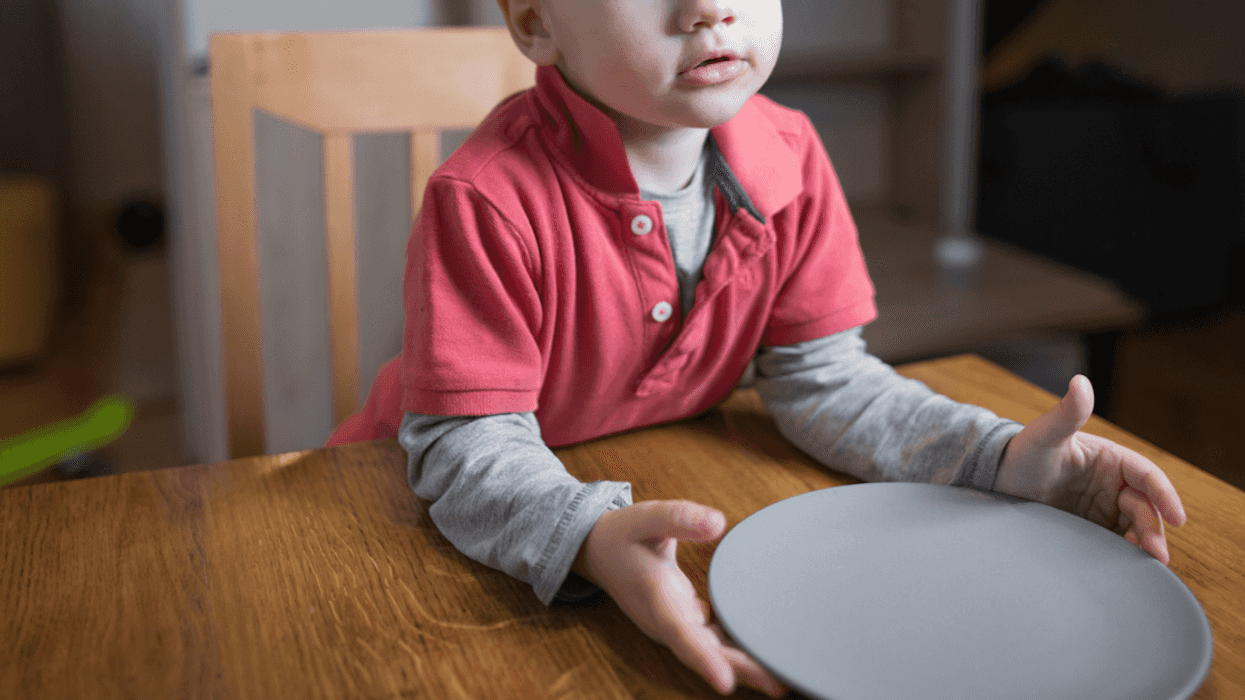 A boy sitting at a table in front of an empty plate.