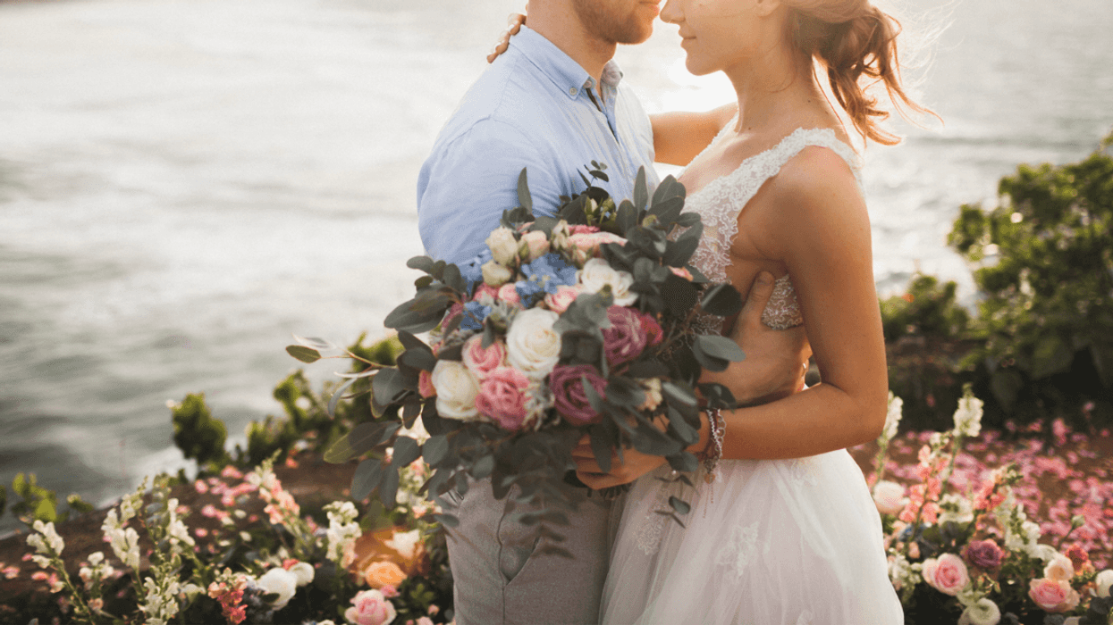 A bride and a groom embracing with the ocean in the background.