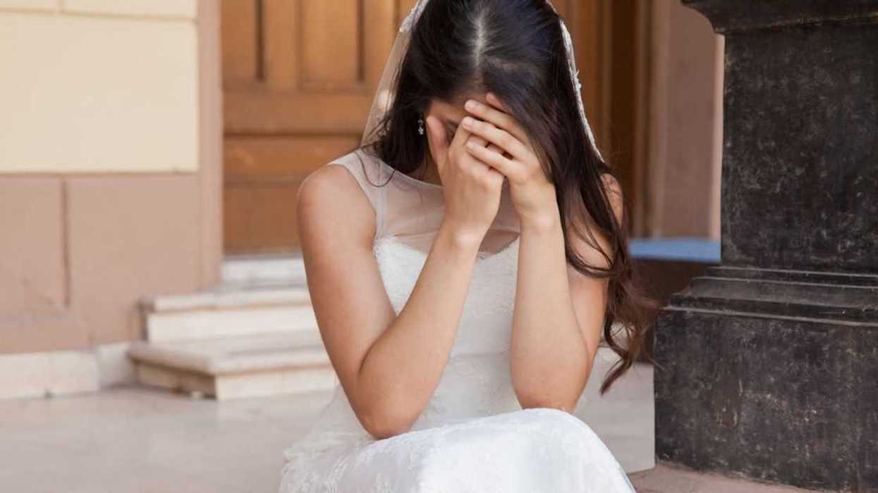 A bride sits on church steps, sad with her head in her hands
