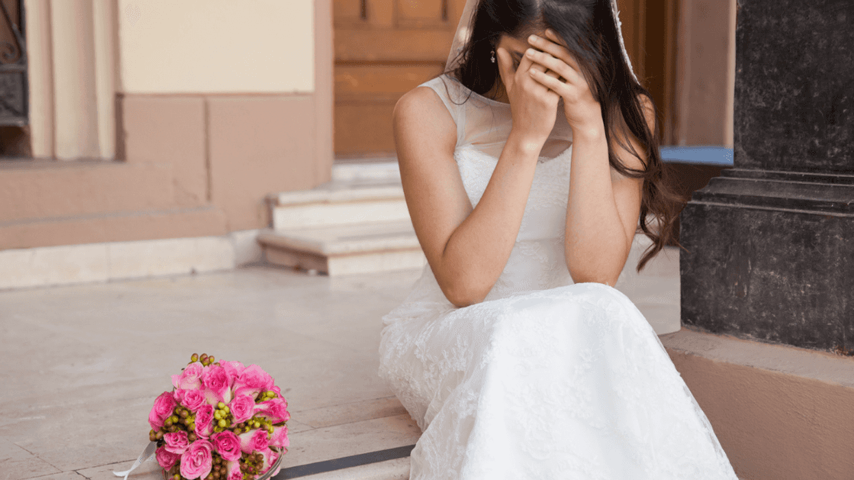 A bride sitting on steps crying into her hands.