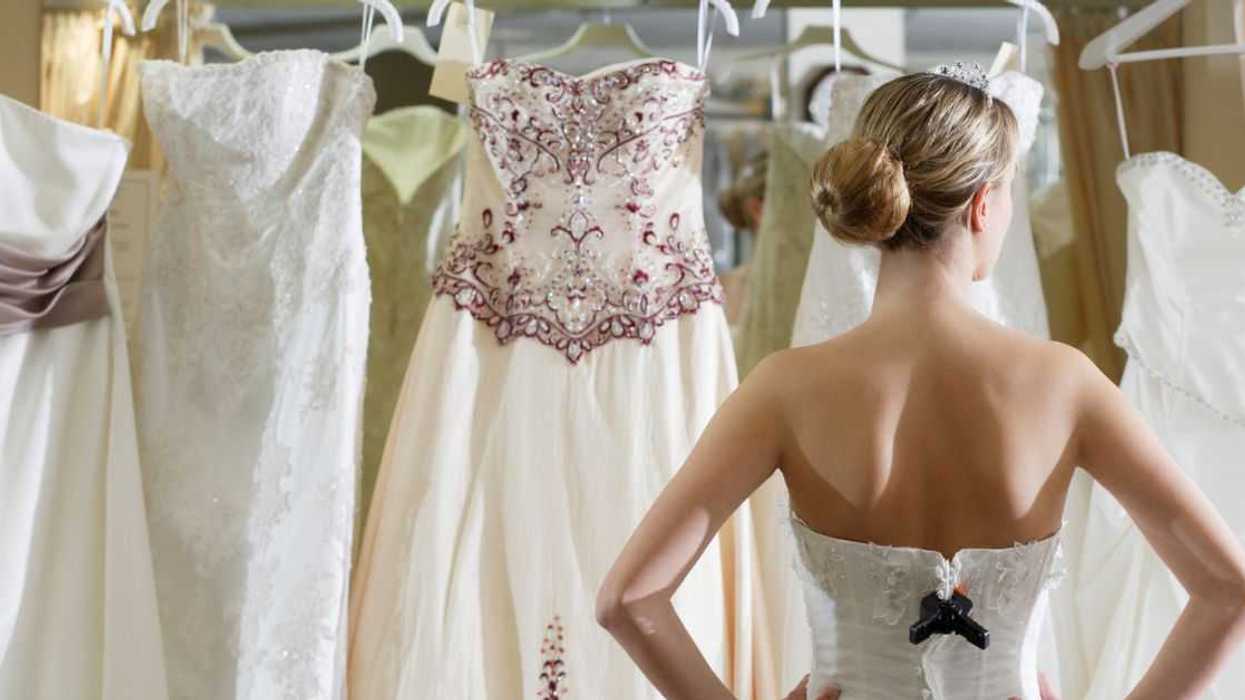 A bride stand before several dresses to choose from