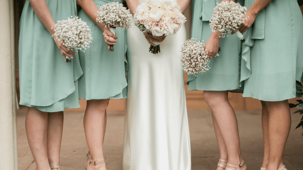 A bride surrounded by bridesmaids in green dresses holding bouquets.