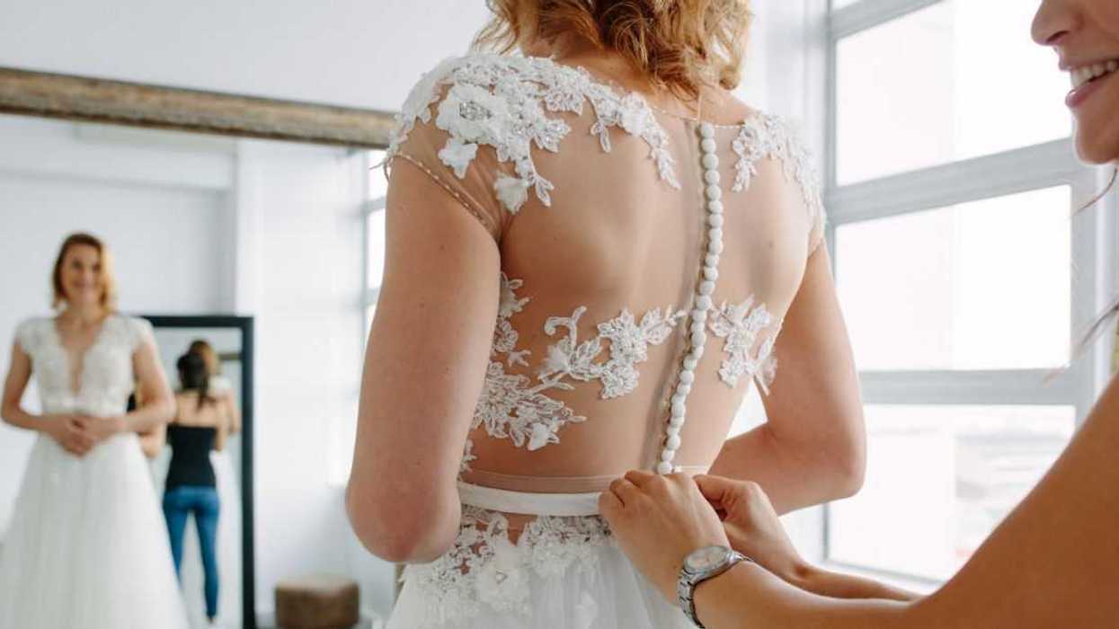 A bride with a dressmaker are making final touch on tailor made gown in bridal clothing shop.