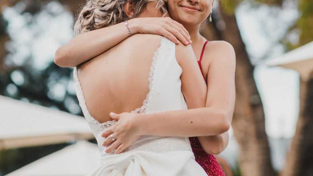 A bridesmaid in a red dress hugs a bride