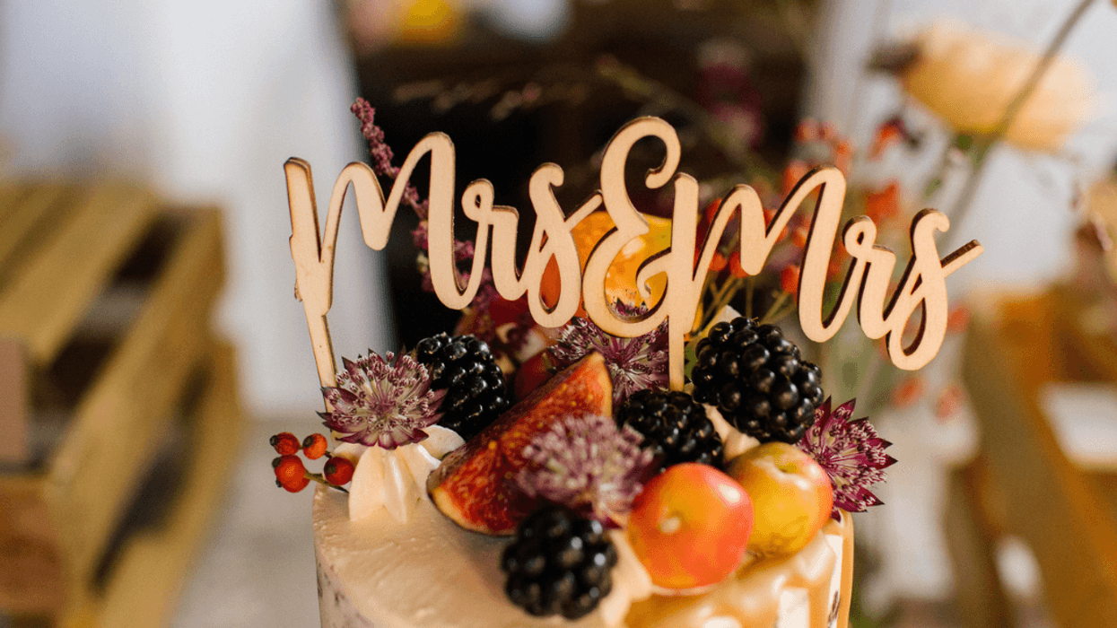 A cake with fruit and a "Mrs & Mrs" cake topper on top.