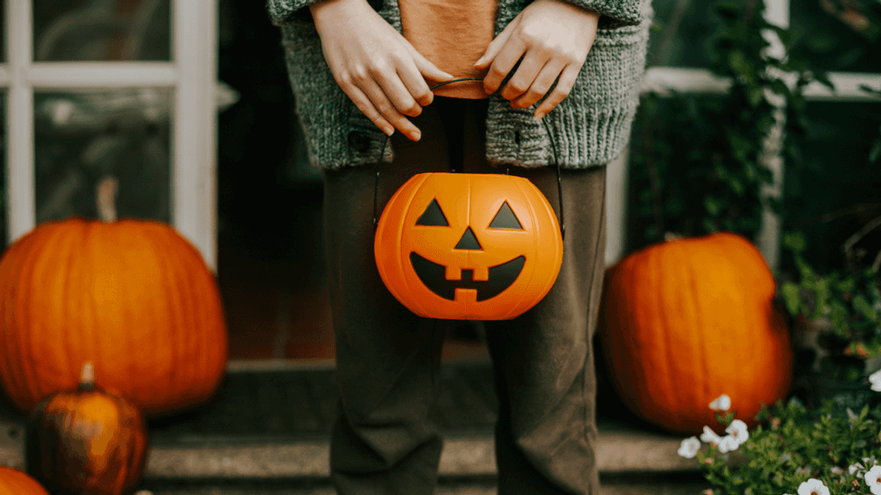 A child holding a jack o'lantern shaped trick or treating bag.