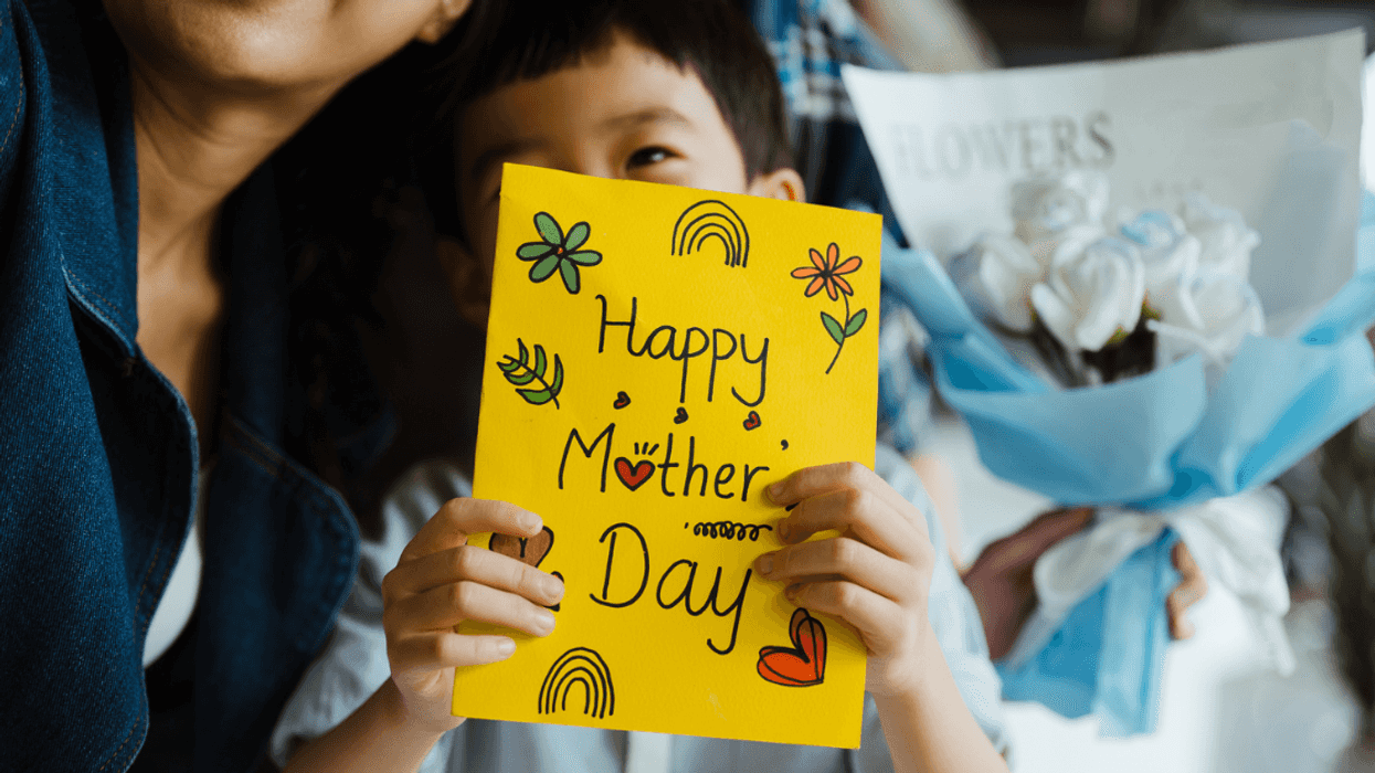 A child holding a mother's day card sitting on a woman's lap.