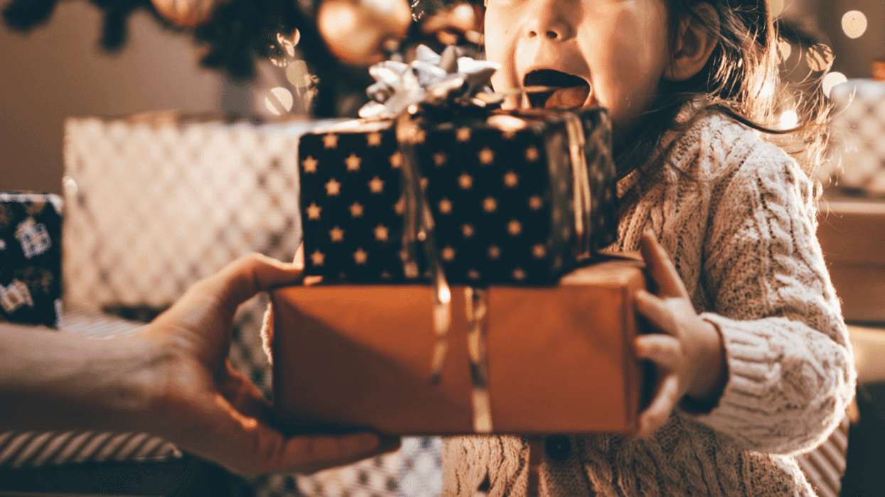 A child holding presents in front of a Christmas tree.
