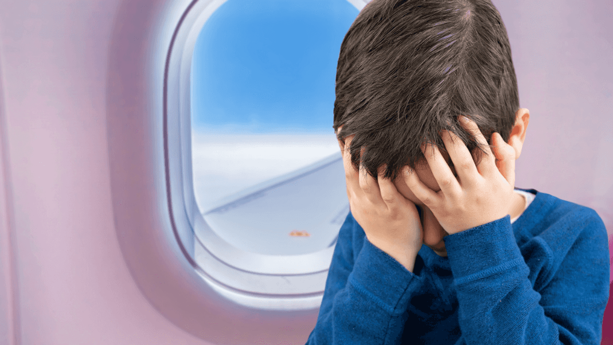 A child in an airline seat with his head in his hands.