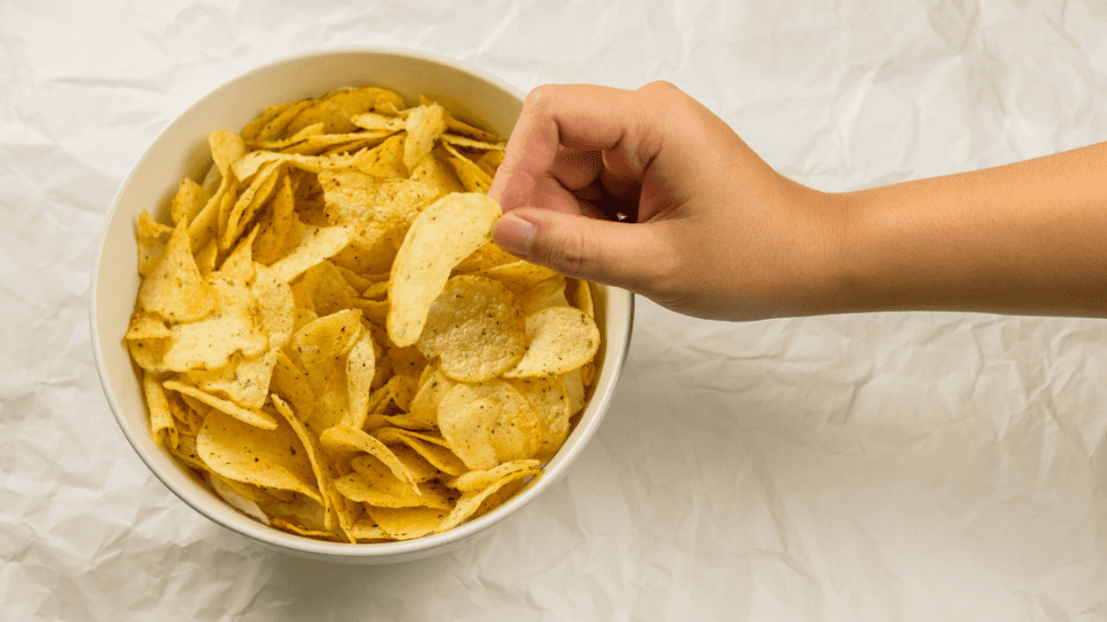 A child's hand taking a potato chip from a bowl.