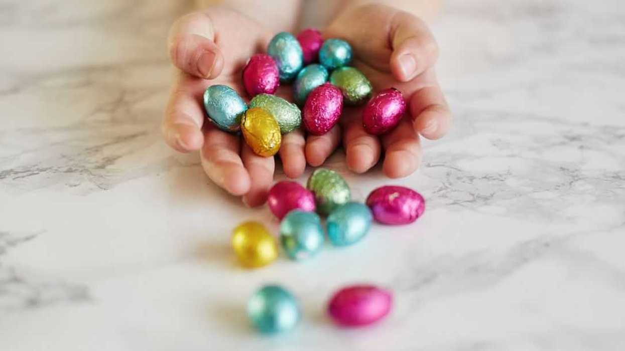 A child's hands holds mini chocolate Easter eggs as they fall out onto a marble counter.