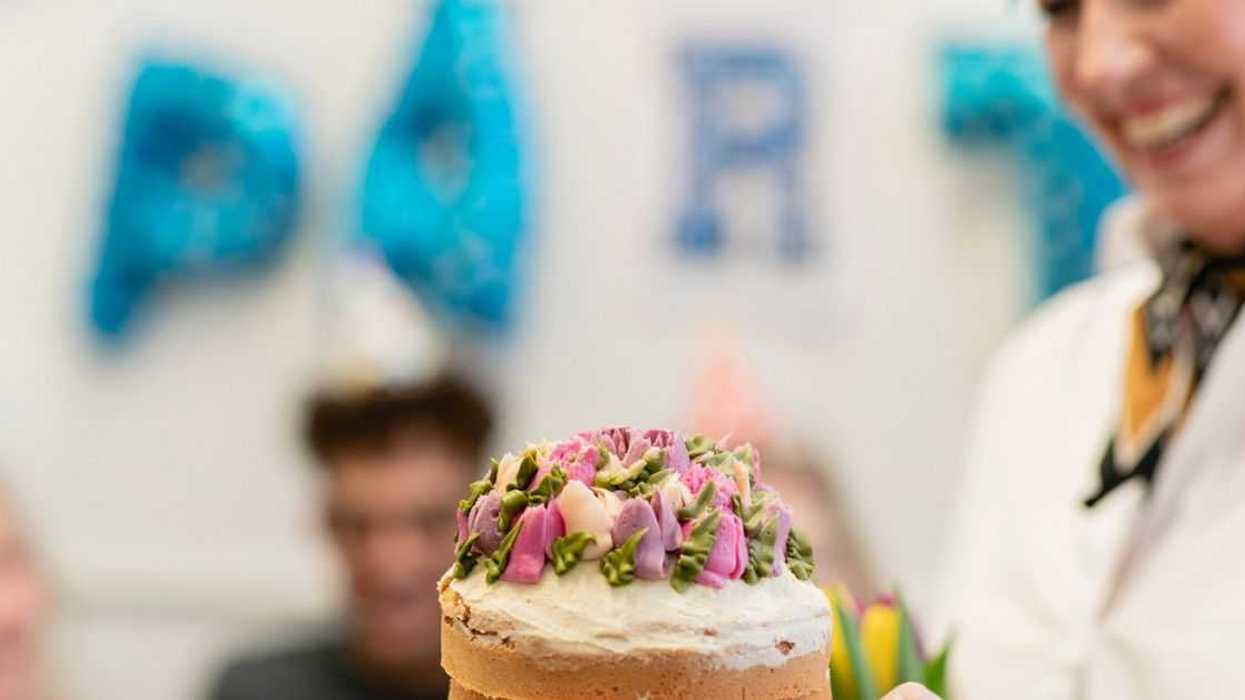 A close-up of an unrecognizable person giving a birthday cake to an unrecognizable woman for her birthday.