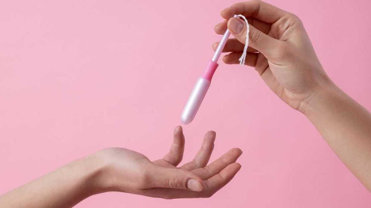 A close up on a pink background with two hands of women passing a tampon in applicator.