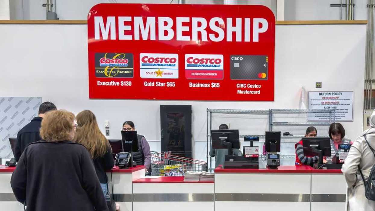 A Costco membership counter where customers are being assisted by employees, with a large sign displaying membership options.