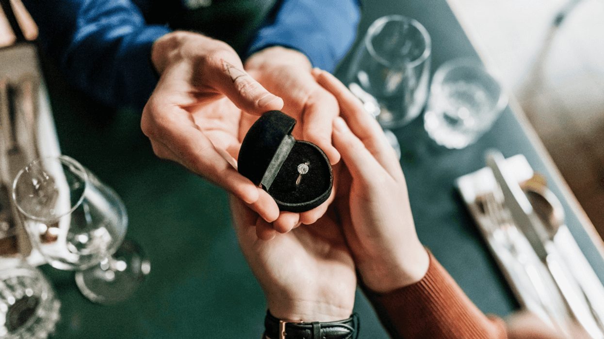 A couple holding an open ring box with an engagement ring inside.
