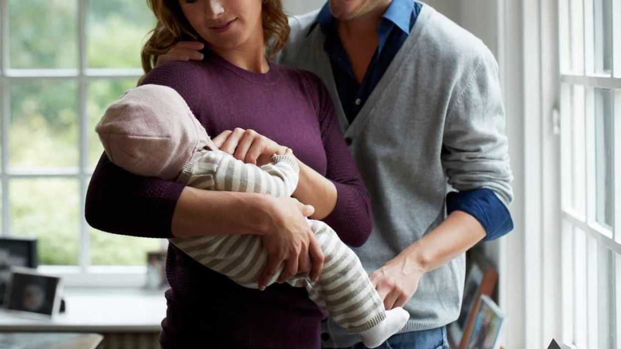 A couple holds their baby and looks on lovingly