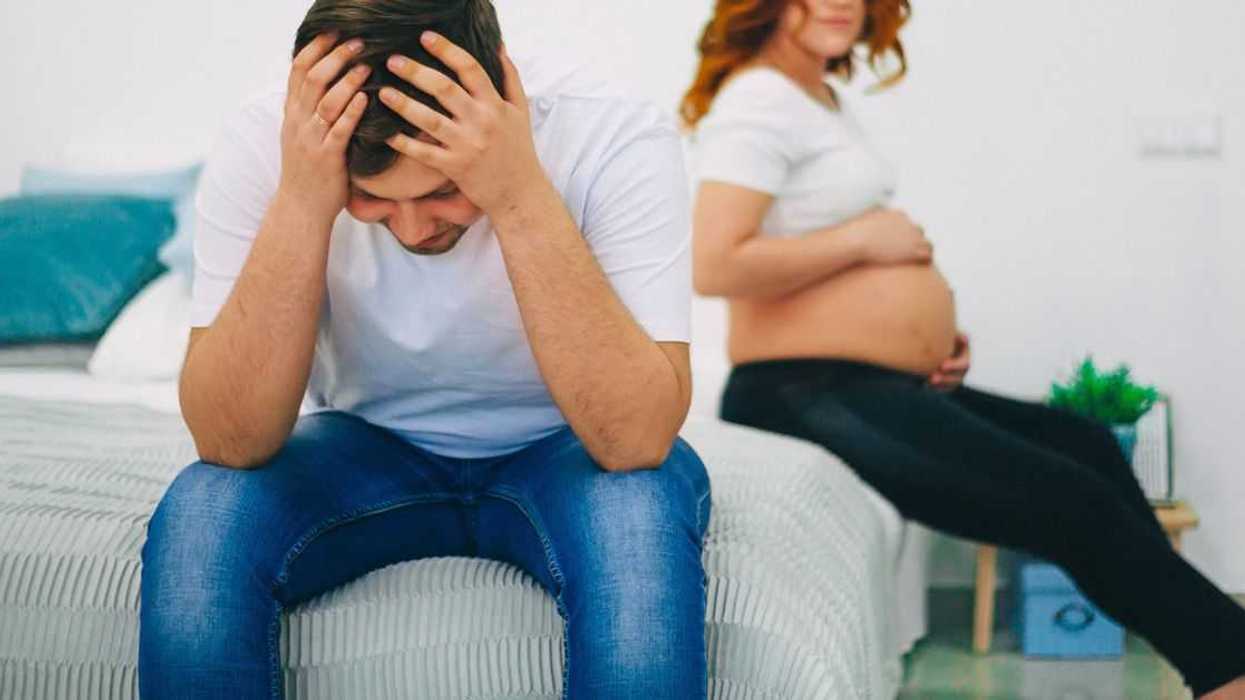 A couple is at odds, they sit on opposite sides of the bed, the woman is pregnant, the man holds his head in his hands