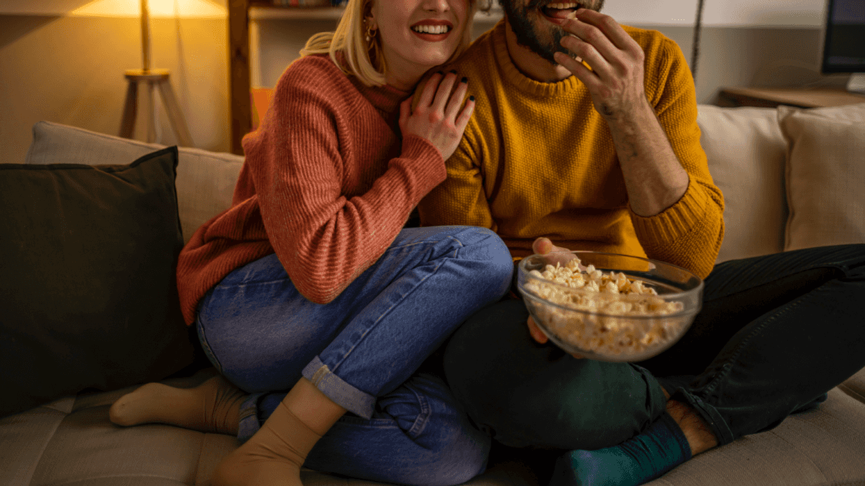 A couple on a sofa watching a movie together and eating popcorn.