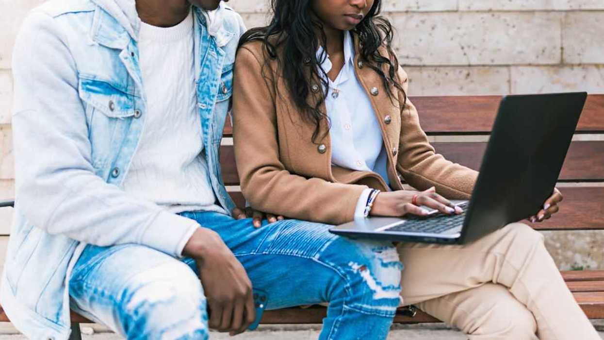 A couple sit on a bench and look at a laptop
