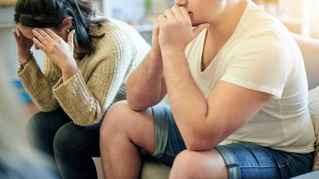 A couple sits on a couch distressed, clearly in the middle of a tense moment