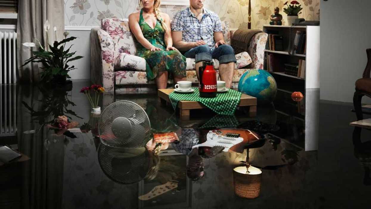A couple sits on a couch in the middle of a messy house