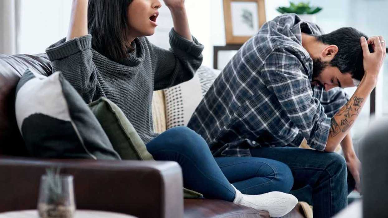A couple sits on the couch watching TV, both seem distraught