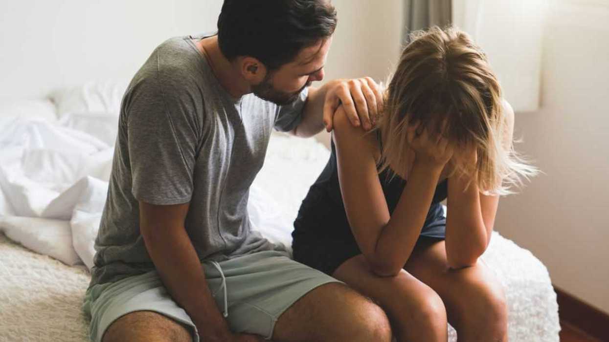 A couple sits on the edge of a bed, in the middle of an argument