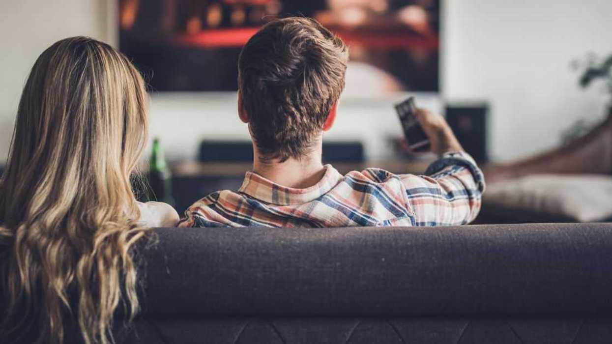 A couple watches a movie, while snuggling on the couch