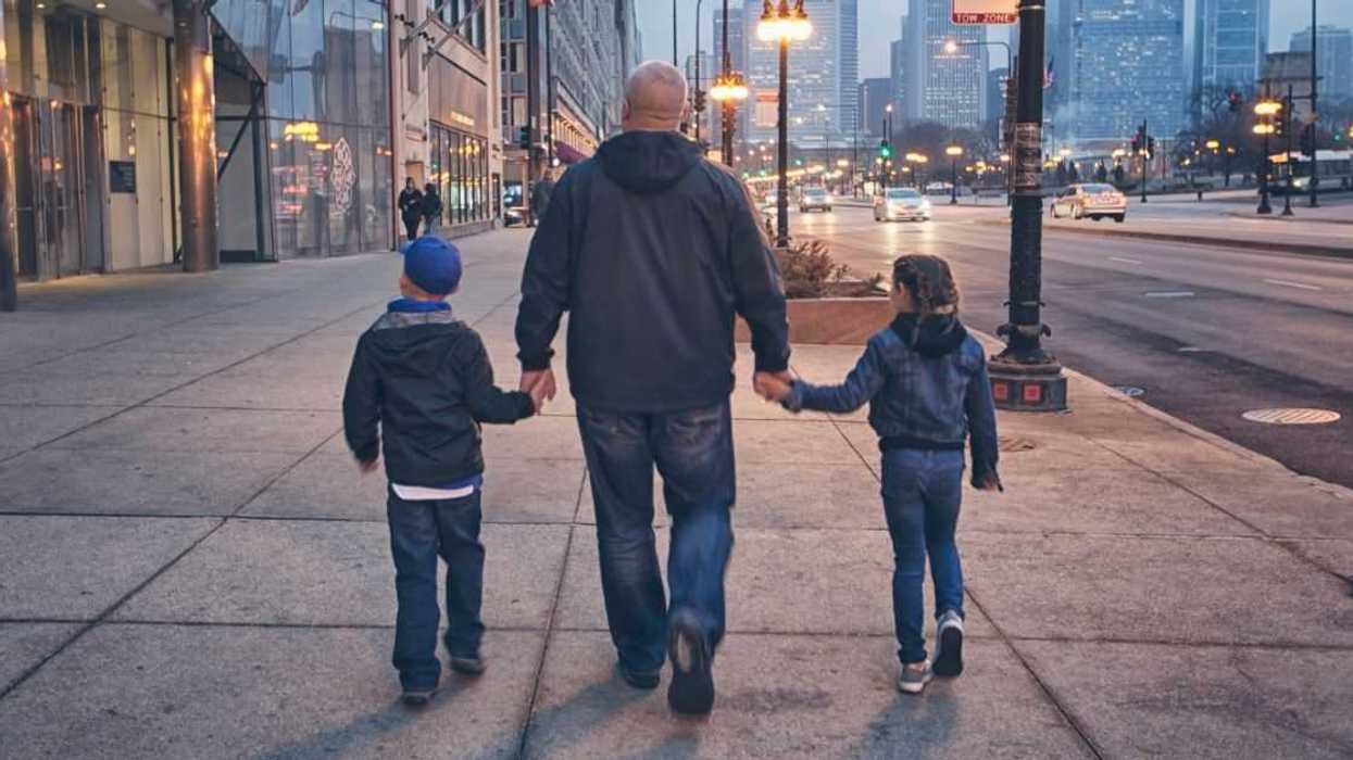 A dad walks away form the camera with his twos sons