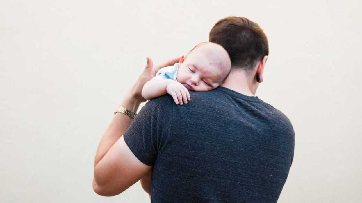 A father shot from behind with his newborn baby over his shoulder facing the camera.