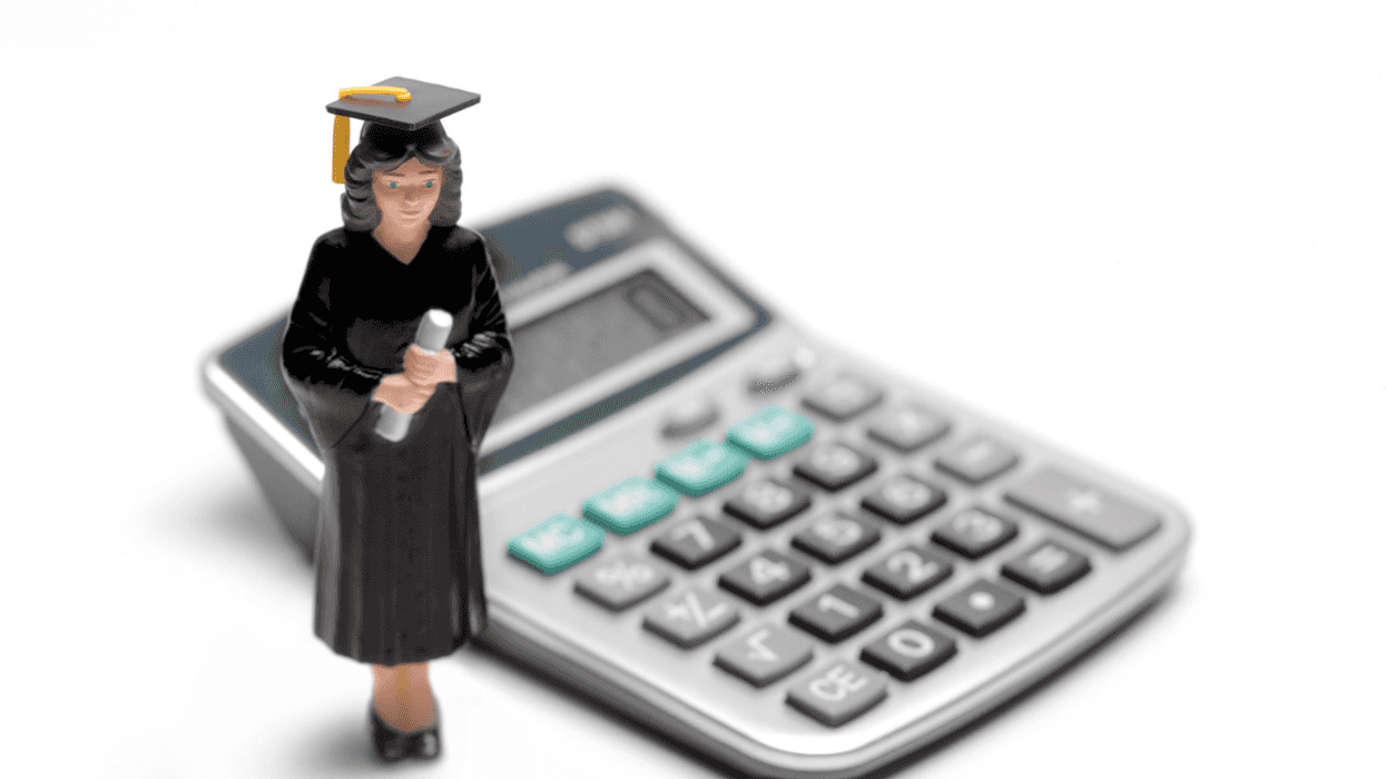 A figurine in a graduation cap and gown placed in front of a calculator.