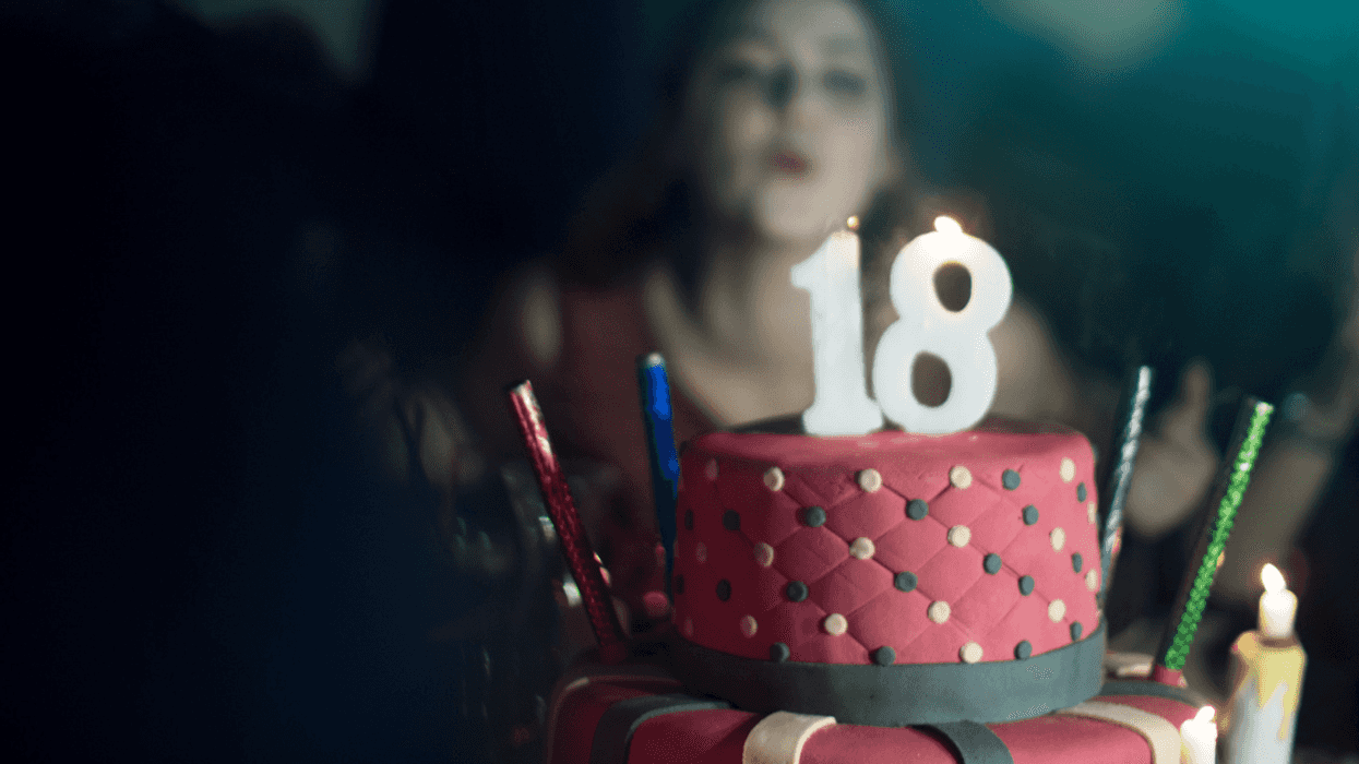 A girl blowing out candles on a cake with the number 18 on the top