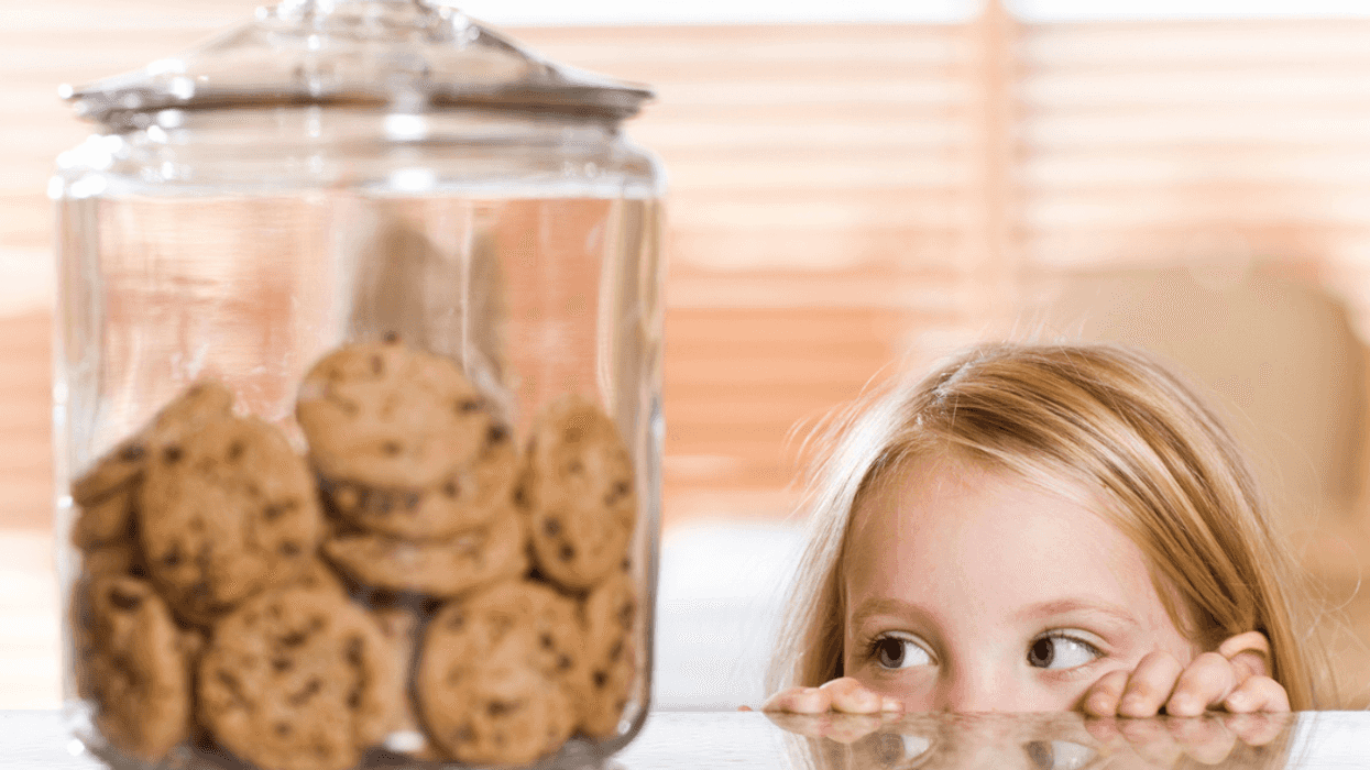 A girl peeking over a counter looking at a cookie jar.