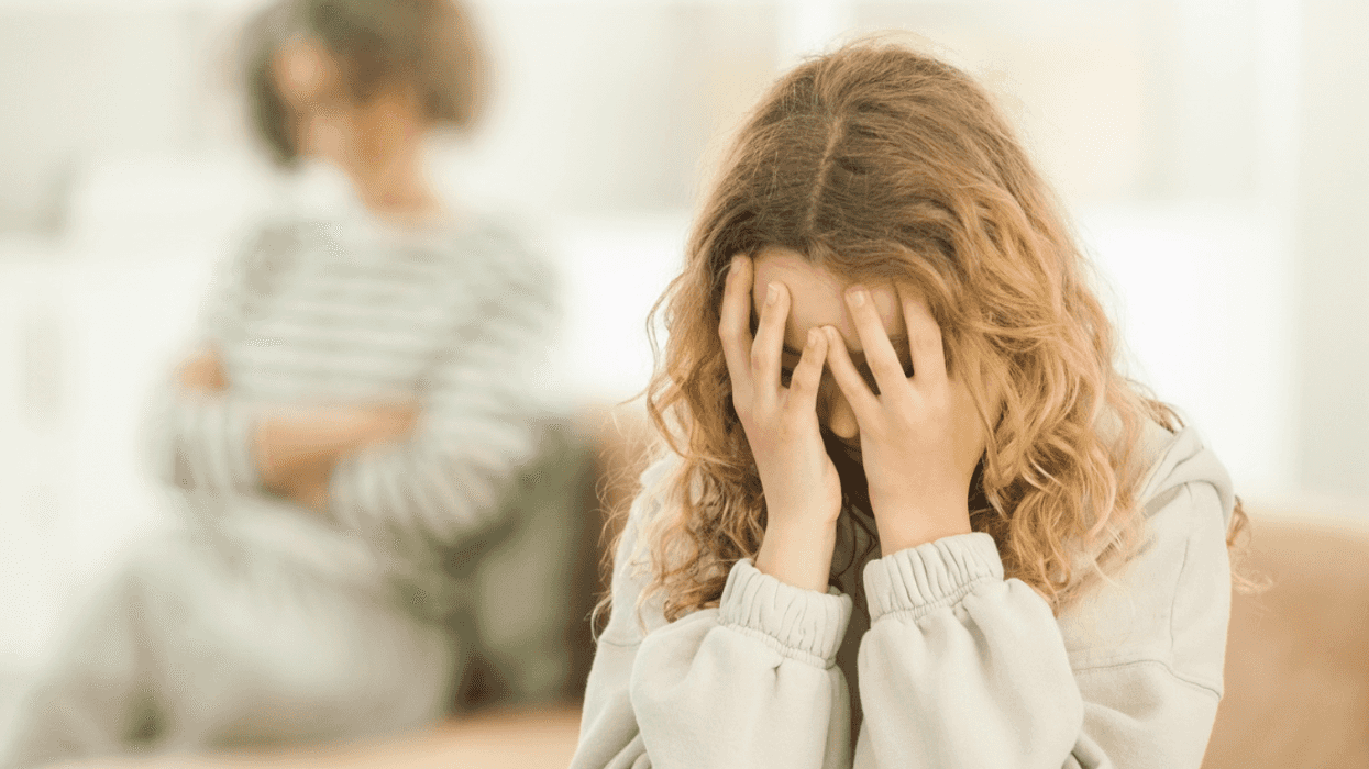 A girl sitting on a sofa with her head in her hands, and a woman sitting behind her.