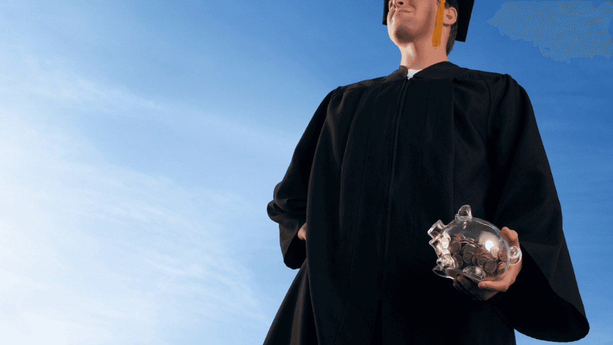 A graduate holding a piggy bank looking off into the sky.