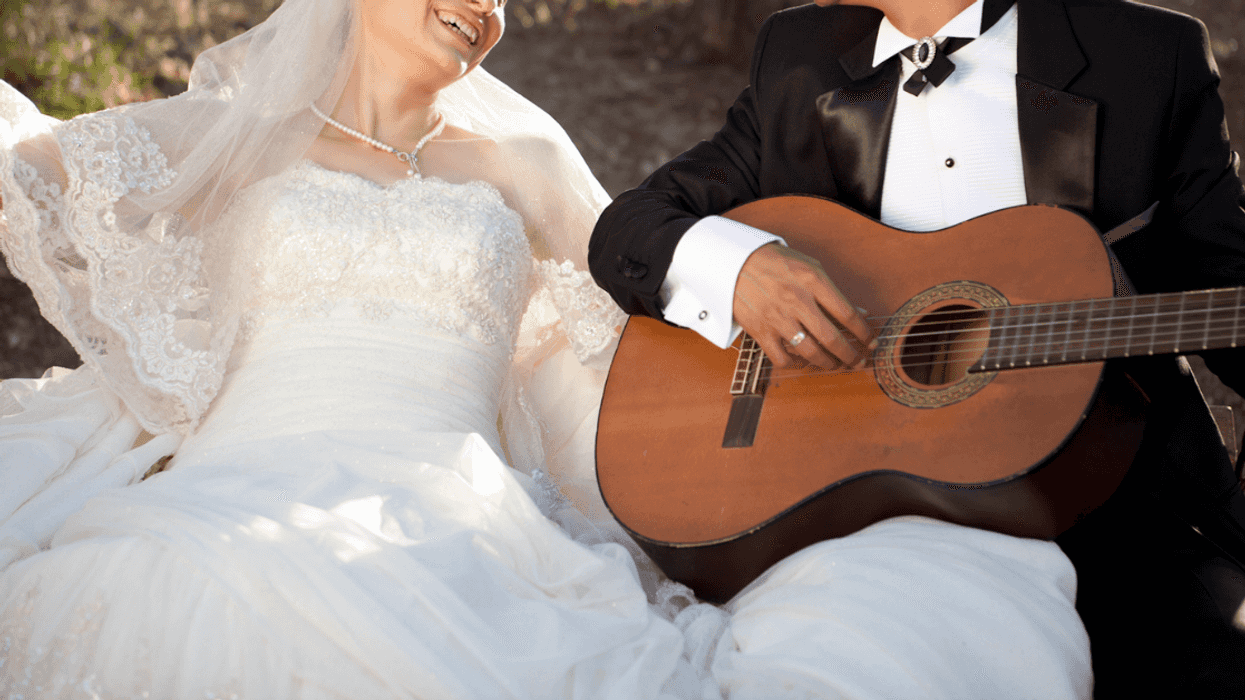 A groom sitting next to a bride, playing the guitar.