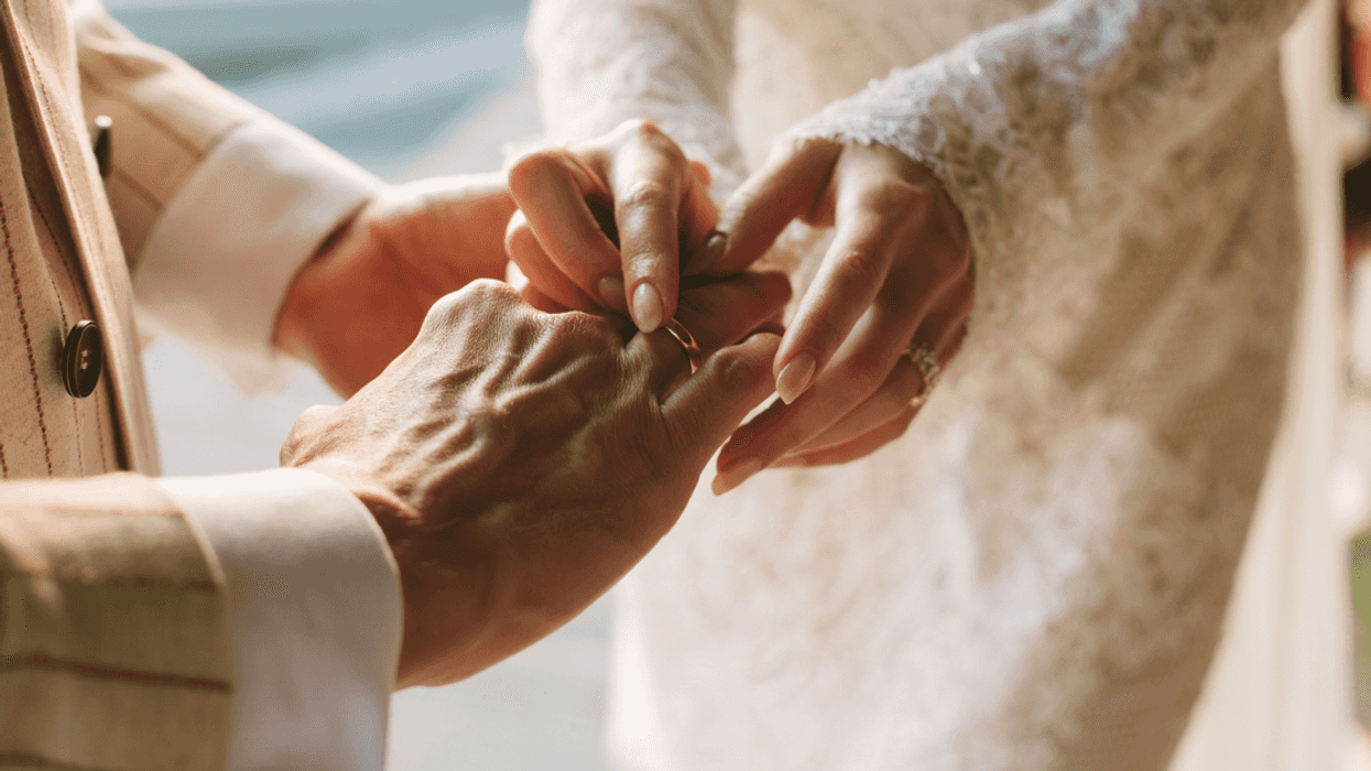 A groom sliding a ring on the finger of a bride.