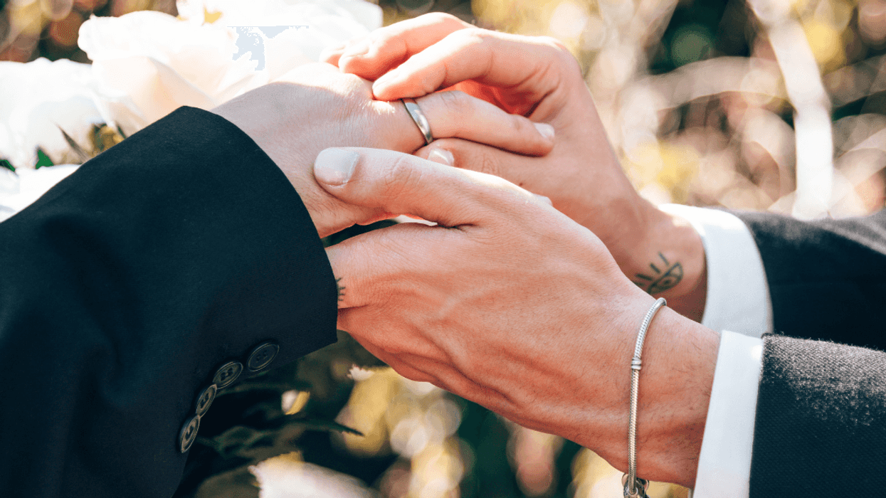 A groom slipping a wedding band on his husband-to-be's finger.