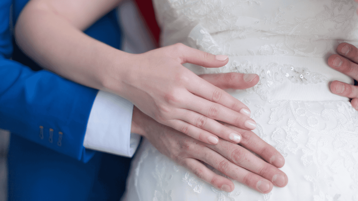 A groom standing behind a bride holding her stomach.