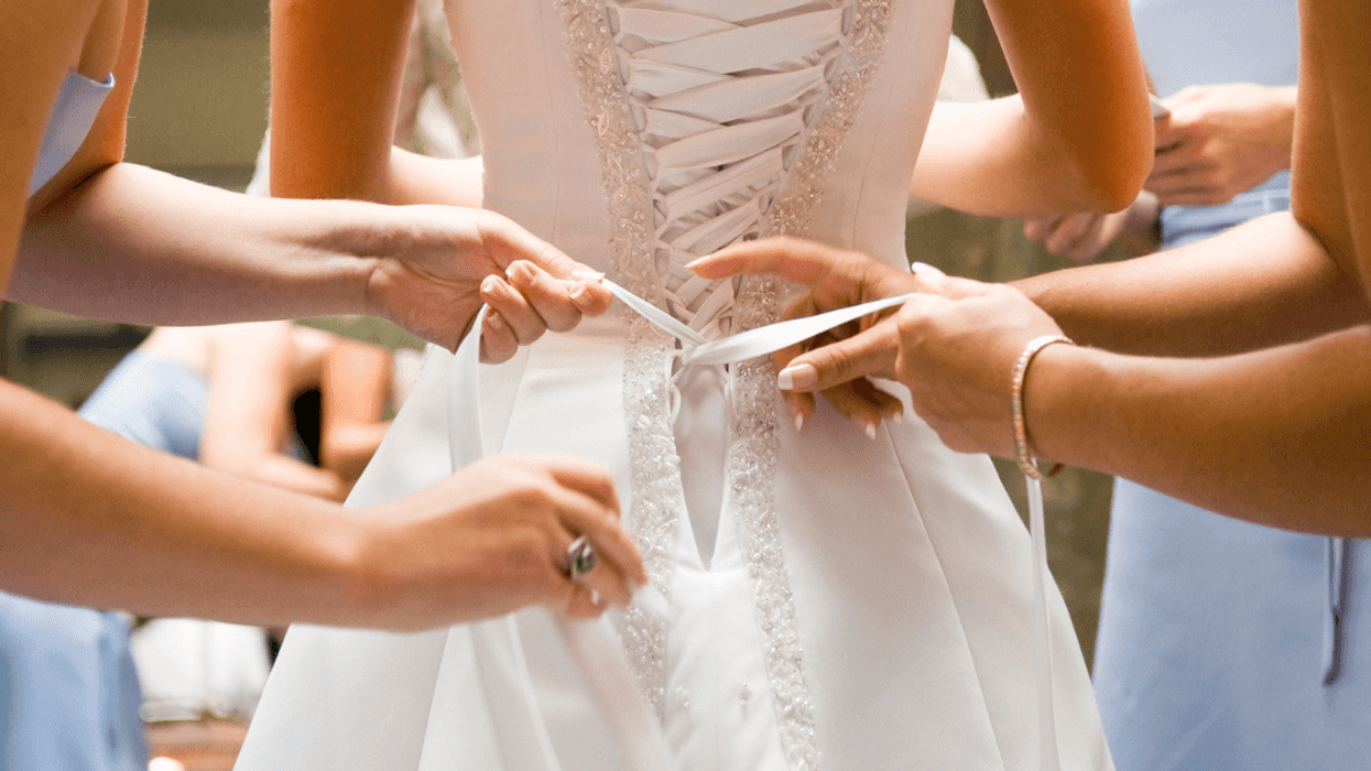 A group of bridesmaids helping a friend lace up her gown.