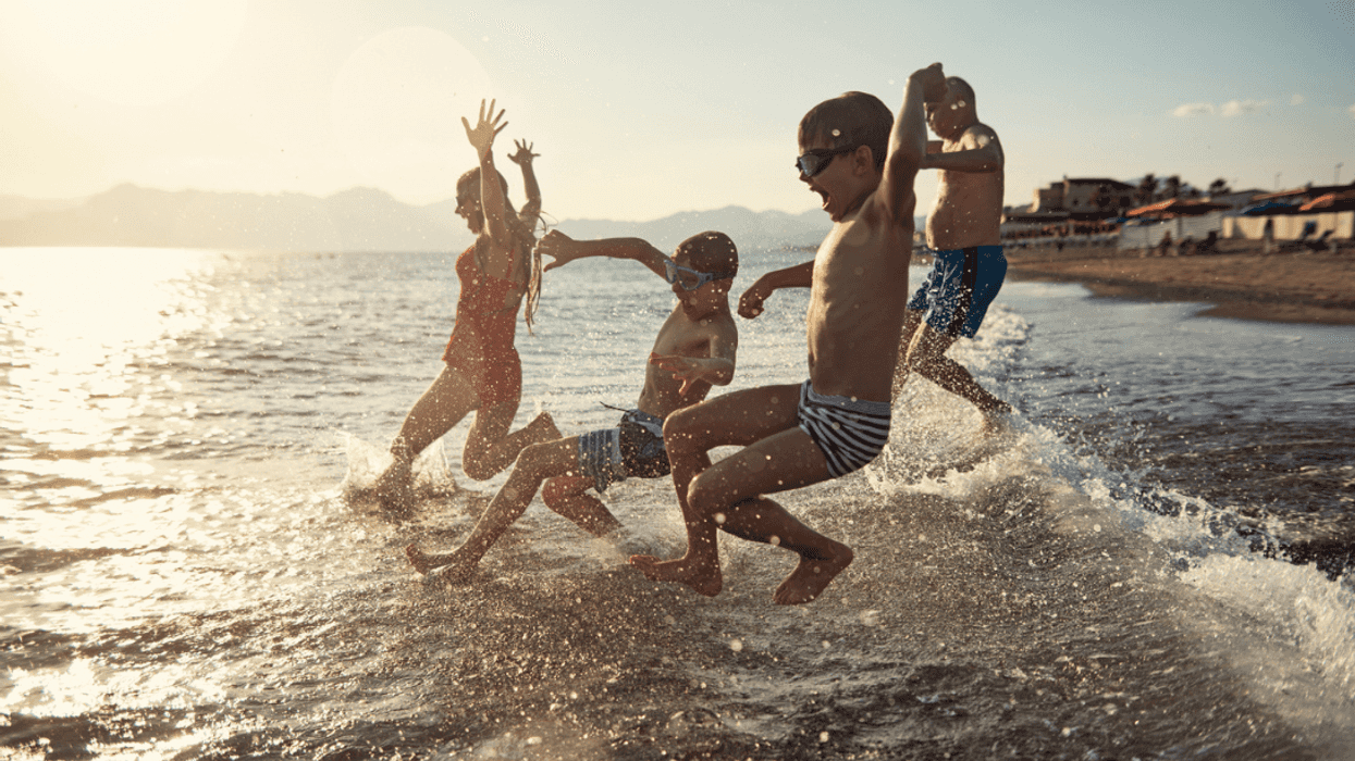 A group of children and an adult man playing in the ocean.