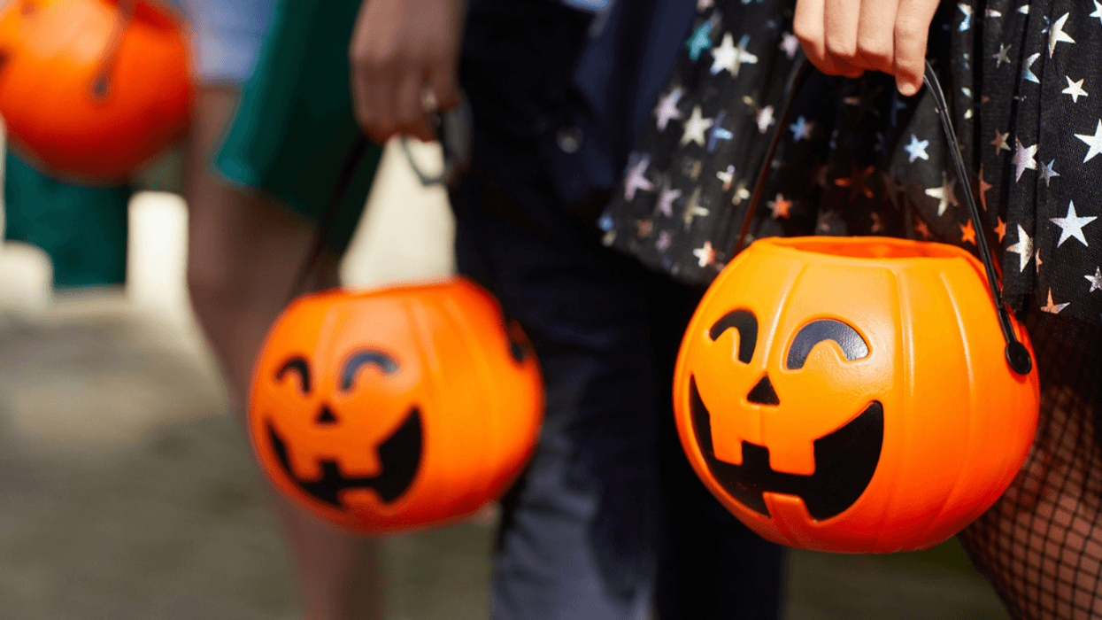 A group of children holding pumpkin trick or treating baskets.
